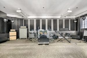 Studio room with drums, amps, keyboard, PA, and sound panels.