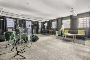 Studio room with drums, amps, keyboard, PA, lounge area, desk, studio monitors, and sound panels.