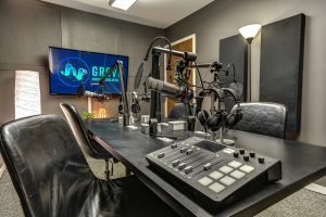 Podcast studio with a Rhodecaster Pro interface, Four Microphones, TV, and RolandGO:LIVECAST for live streaming.