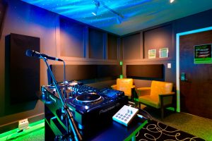DJ Studio featuring Pioneer CDJs, color changing lights, automated recording, live-streaming capabilities, chairs, and microphones.